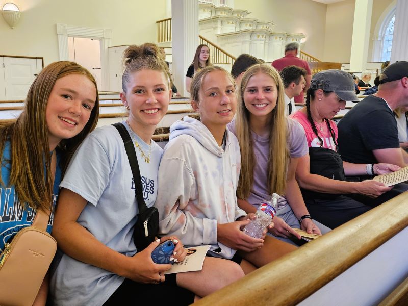 Four young women smile while seated on a bench in the Kirtland Temple.