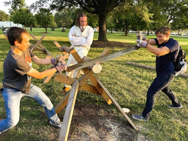 Two young men work together to saw a log by hand.